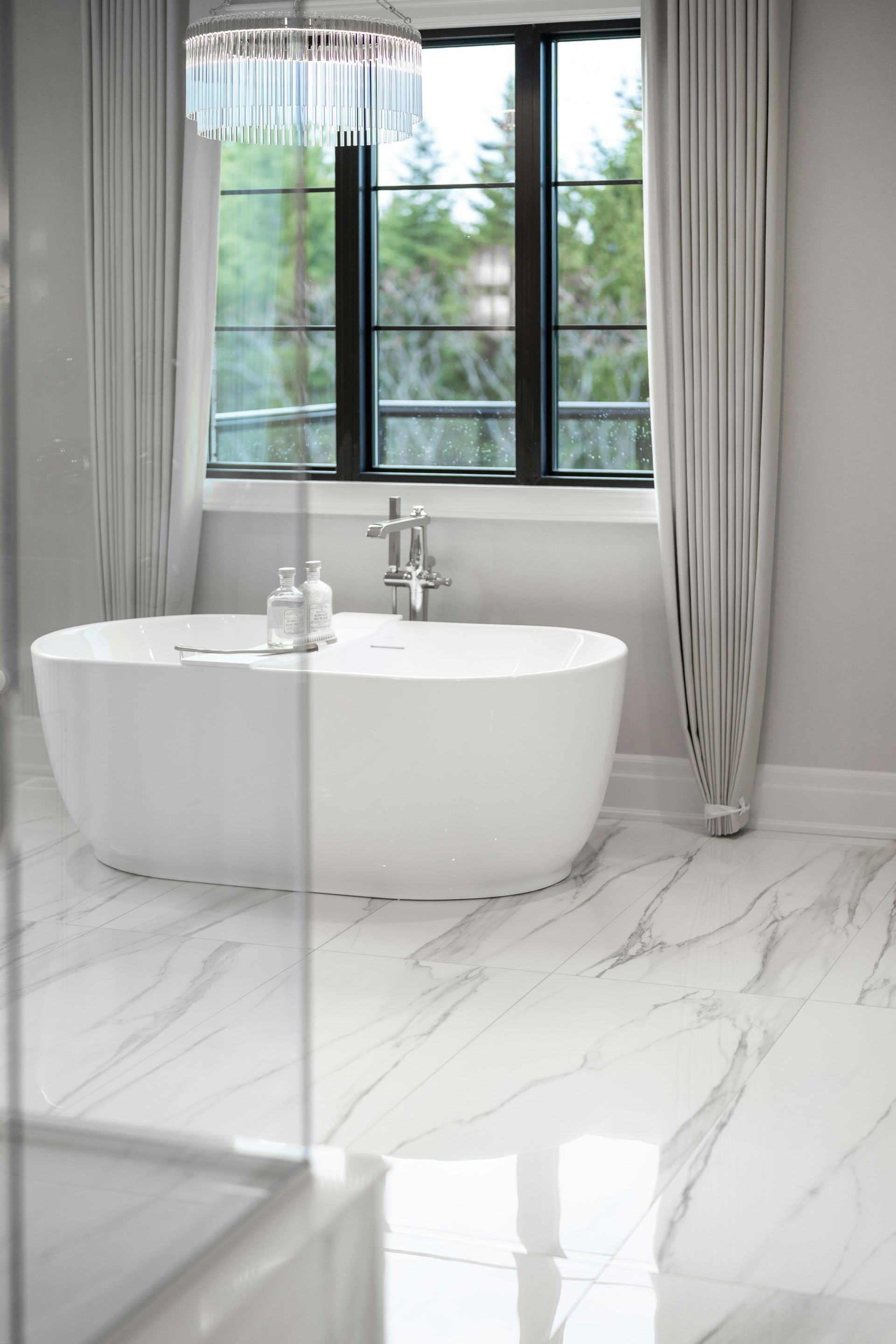 Modern bathroom with a white freestanding bathtub and large window.